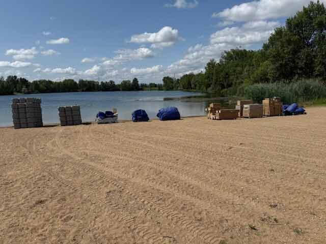 Matériaux livrés par Cargomatic pour installation nautique, palettes et modules alignés sur sable au bord de l’eau.