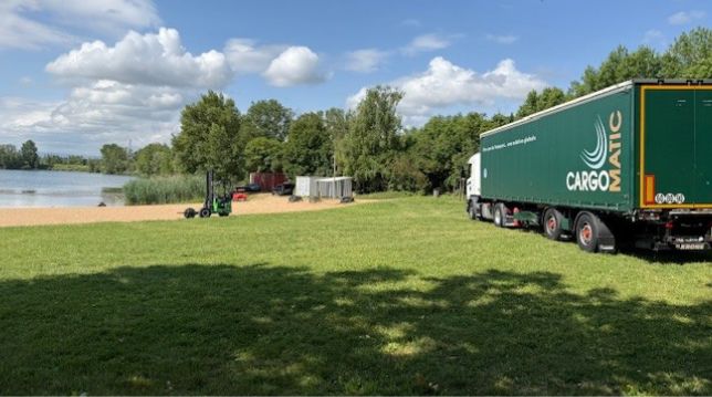 Camion Cargomatic avec chariot embarqué livrant sur un site au bord d’un lac, livraison directe sur chantier en pleine nature.