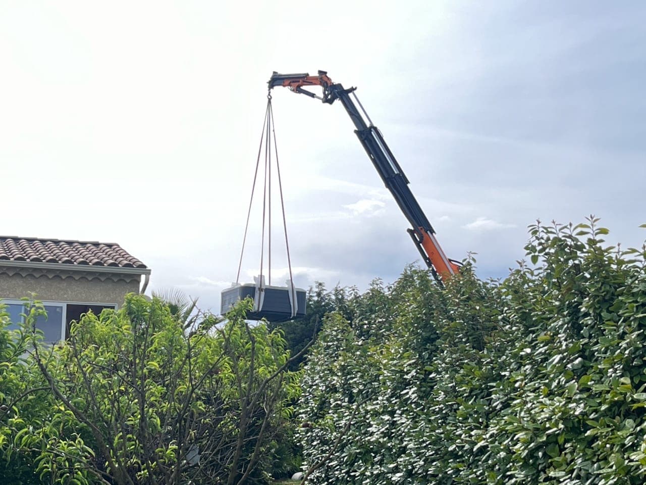 Livraison d'un spa directe domicile en le passant par dessus une haie grâce à un camion grue Cargomatic